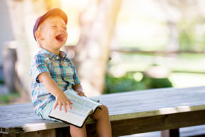 Laughing boy on a bench reading a book